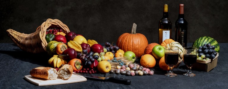 Cornucopia overflowing with fruit and vegetables; two glasses of wine; pumpkin