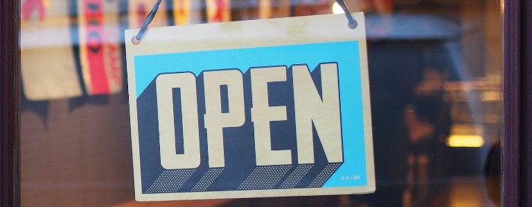 A blue 'Open' sign hanging up on a storefront door