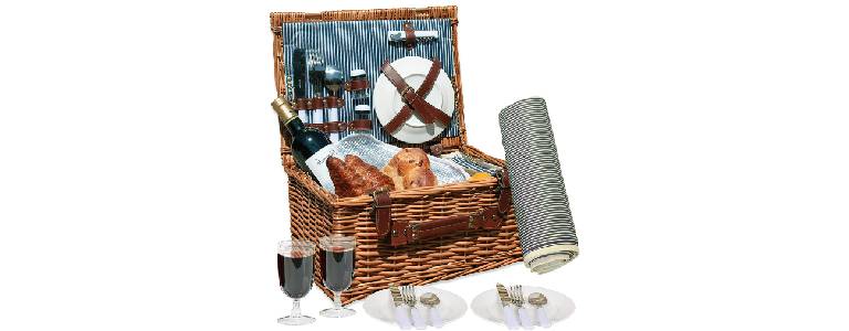 A wicker picnic basket filled with tableware, a bottle of wine and pastries