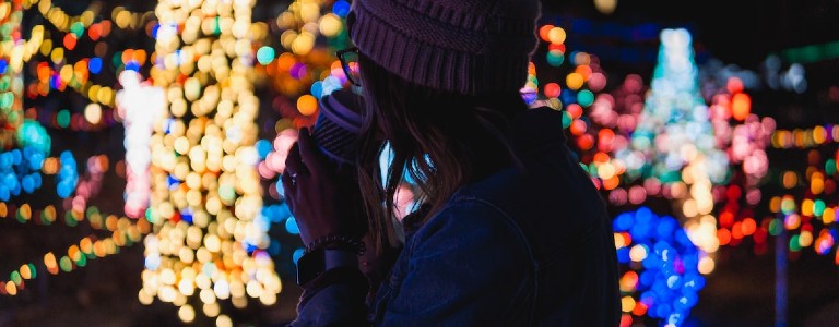 Woman drinking cup of coffee while watching outdoor holiday lights
