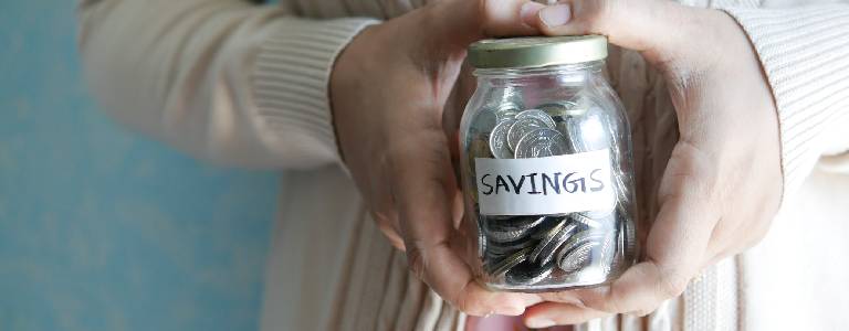 Woman holding a jar of coins with the label 'Savings' on it.