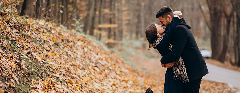 Couple hugging each other while standing in fallen autumn leaves
